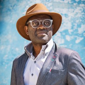 Portrait of Alain Mabanckou against a cloud backdrop
