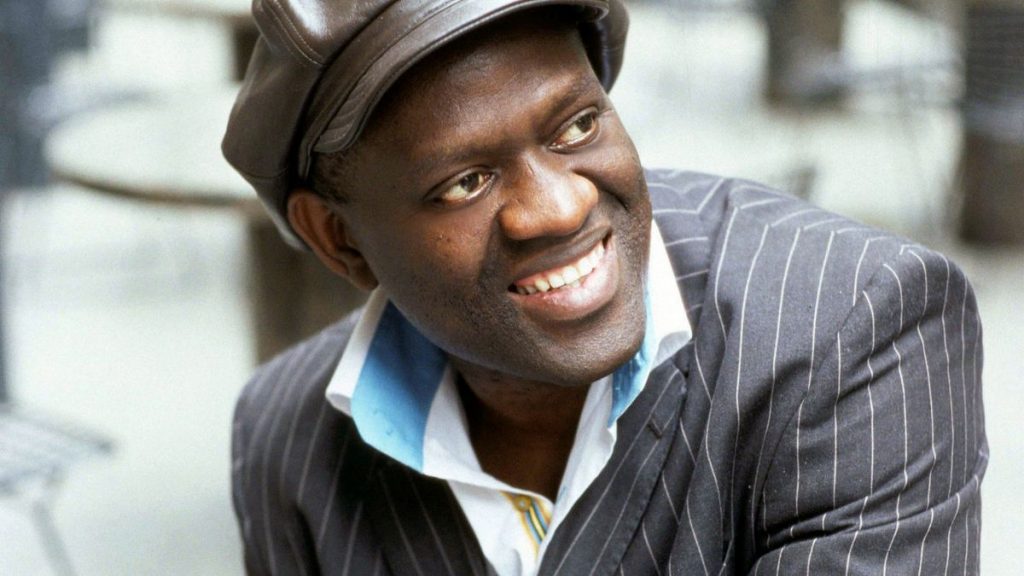 Alain Mabanckou looks away from the camera and smiles in a close-up shot