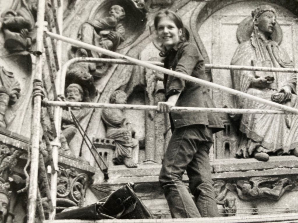 Diane Brouillette poses on some scaffolding by a stone relief in a black-and-white photo