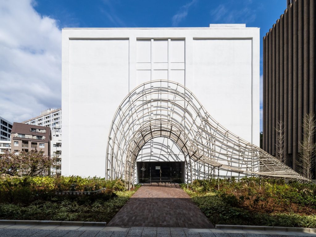 Waseda International House of Literature in Tokyo, an imposing white structure with whimsical curved scaffolding around the entrance, is shown