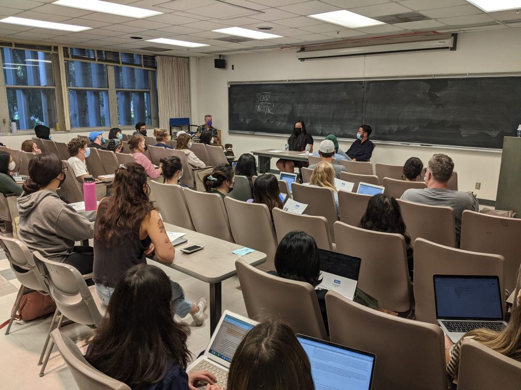 Photo of a classroom from behind. The backs of students' heads are visible.
