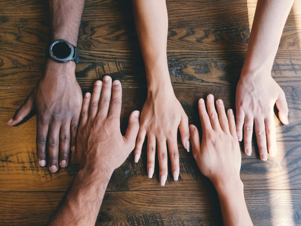 Five hands with different skin tones on a wooden table