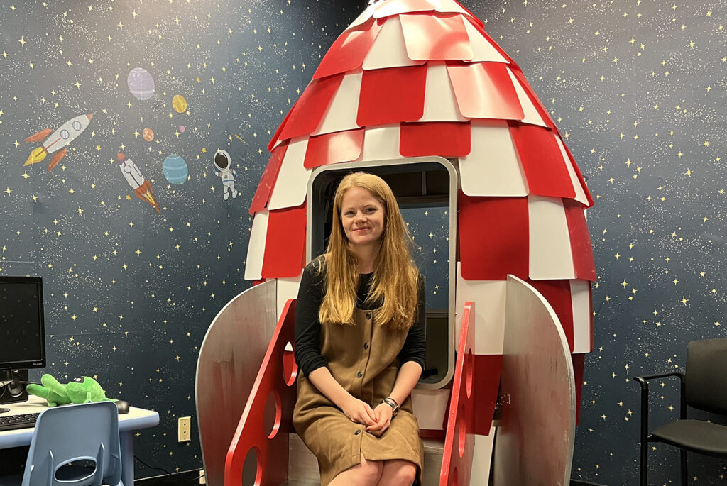 Meg Cychosz sitting in a model rocket ship in her research lab