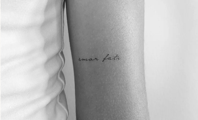 Tattoo of the phrase amor fati on a person's forearm
