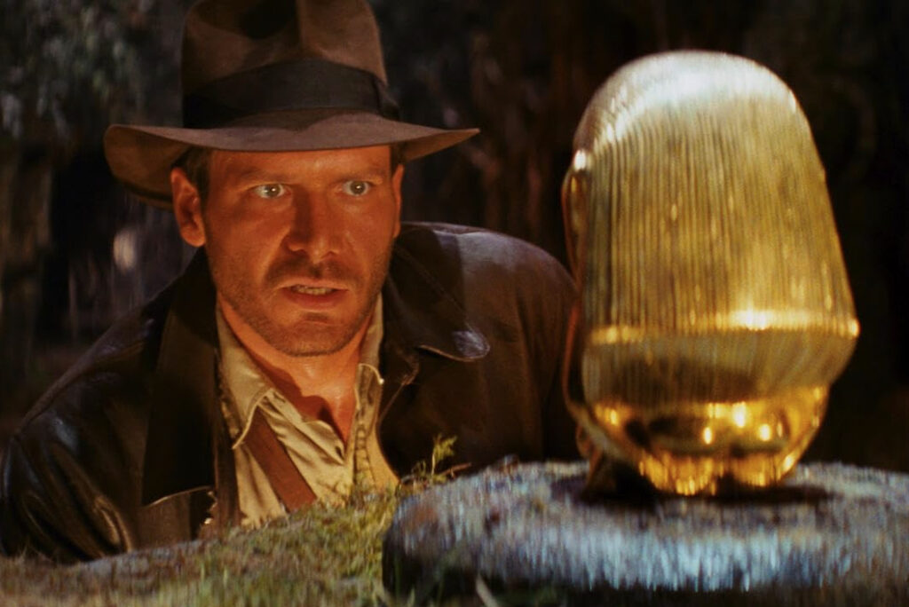 Harrison Ford as Indiana Jones looking at golden idol in still image from Raiders of the Lost Ark movie
